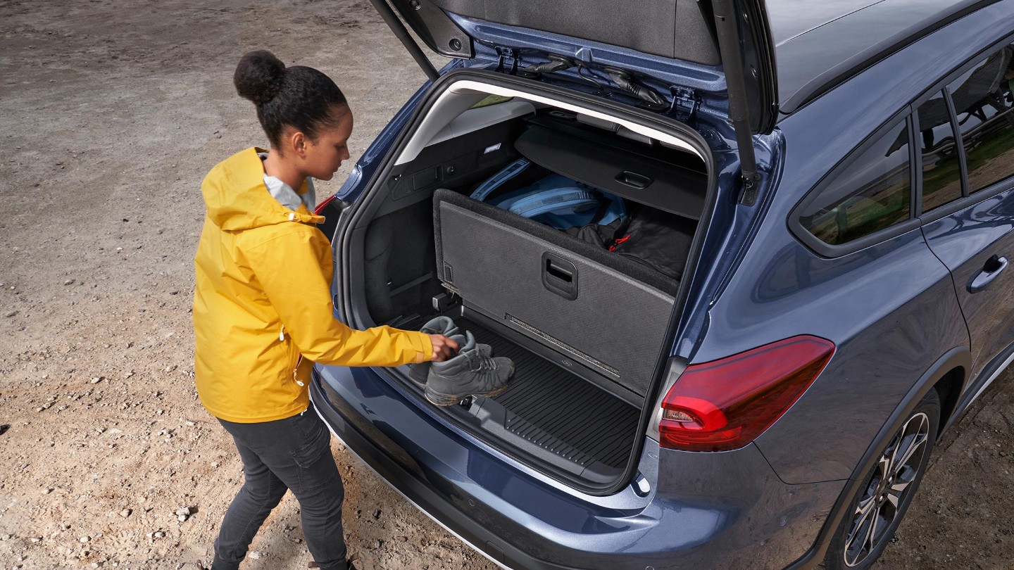 Ford Focus Active blu. Vista posteriore a tre quarti dall’alto. Una donna inserisce degli oggetti nel bagagliaio.