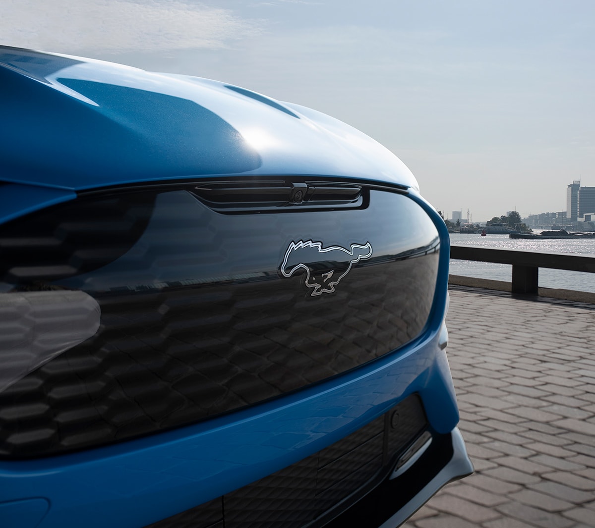 Ford Mustang Mach-E GT blu. Vista frontale a tre quarti con dettaglio del pony Mustang.