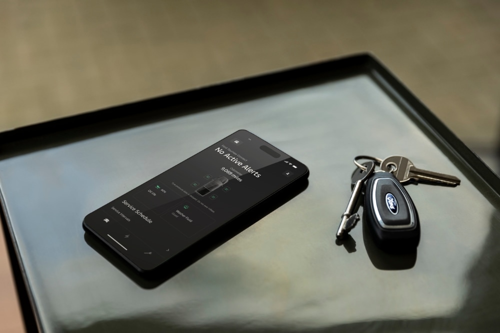 Uno smartphone mostra la Ford App con lo stato del veicolo, accanto a una chiave Ford.