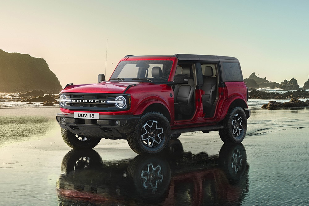 Vista laterale di un Ford Bronco rosso senza portiere, parcheggiato su una spiaggia di sabbia bagnata.