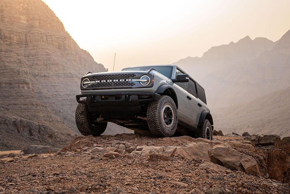 Un Ford Bronco grigio parcheggiato su un sentiero roccioso in uno scenario montano.