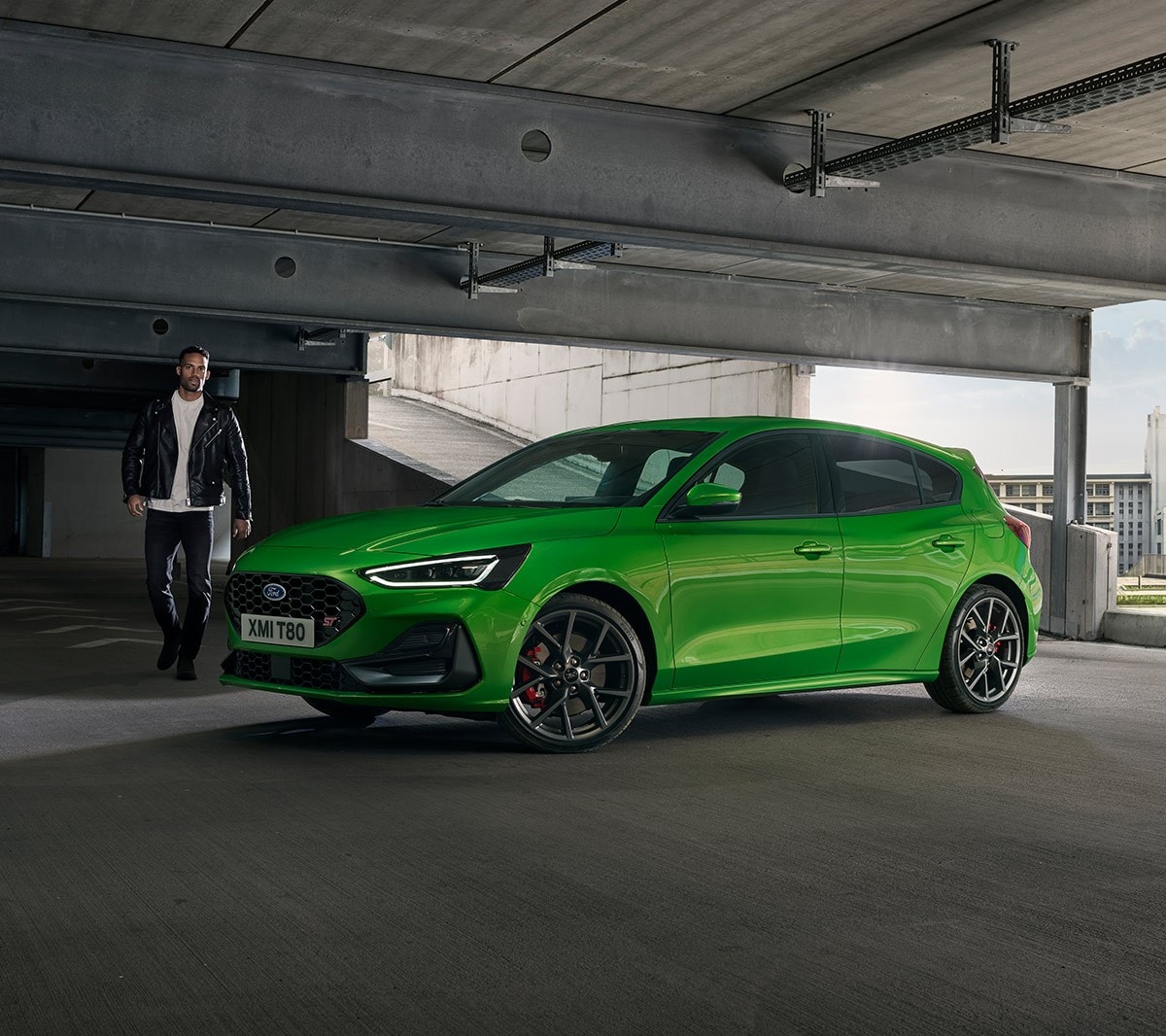 Ford Focus ST verde. Vista frontale a tre quarti, in marcia su una strada extraurbana.