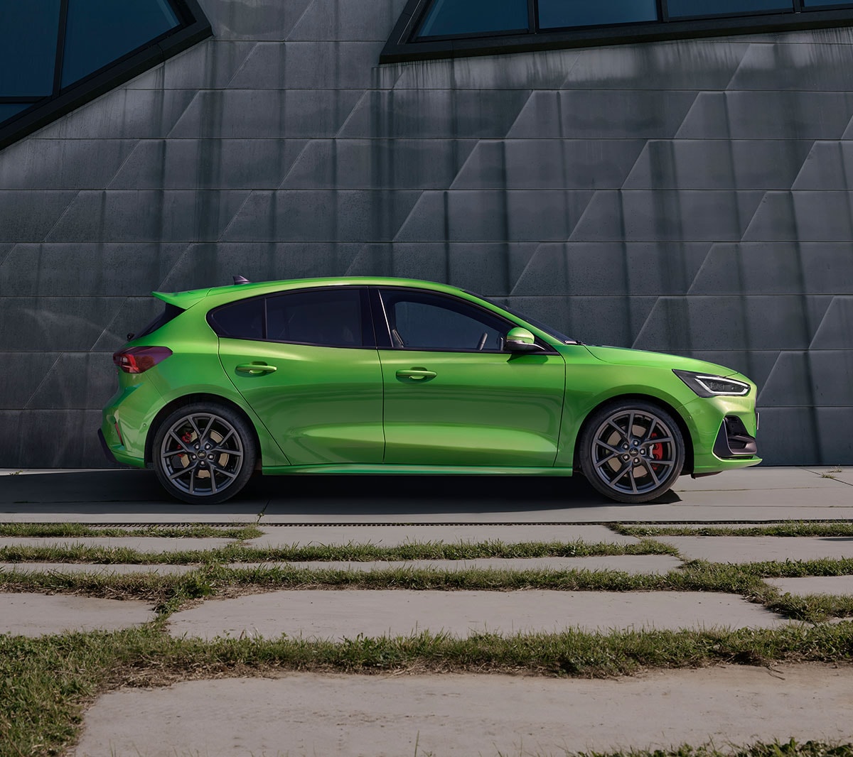 Ford Focus ST verde. Vista laterale, ferma davanti a una parete grigia.