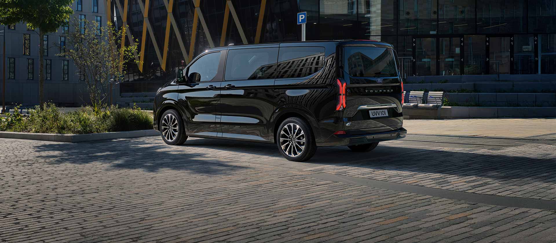 Ford E-Tourneo Custom nera, vista laterale e posteriore davanti a un edificio moderno
