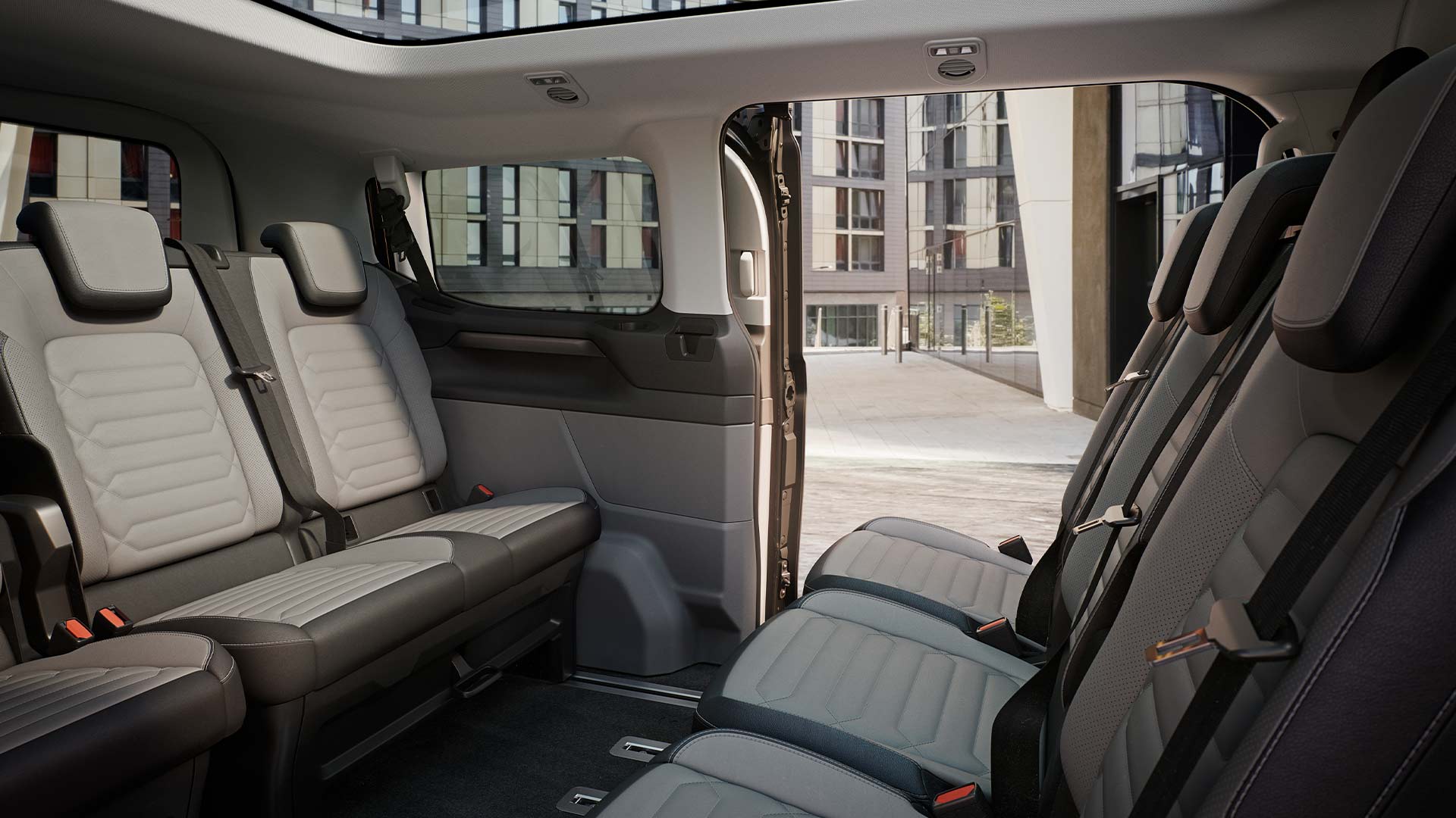 Interni della Ford Tourneo Custom con diverse file di sedili grigi e tetto panoramico