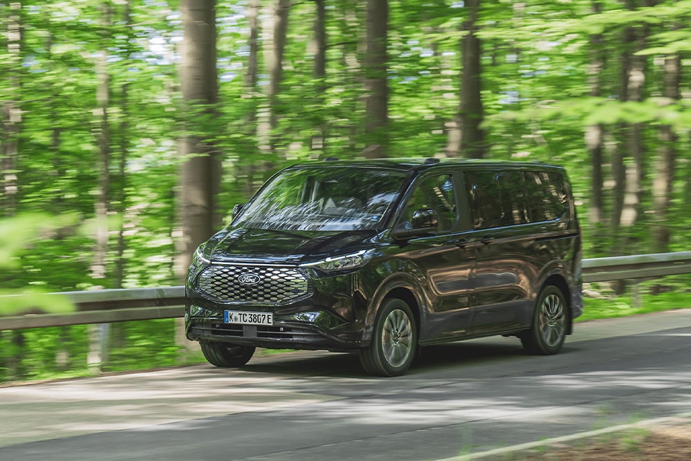 Ford E-Tourneo Custom nera che percorre una strada alberata