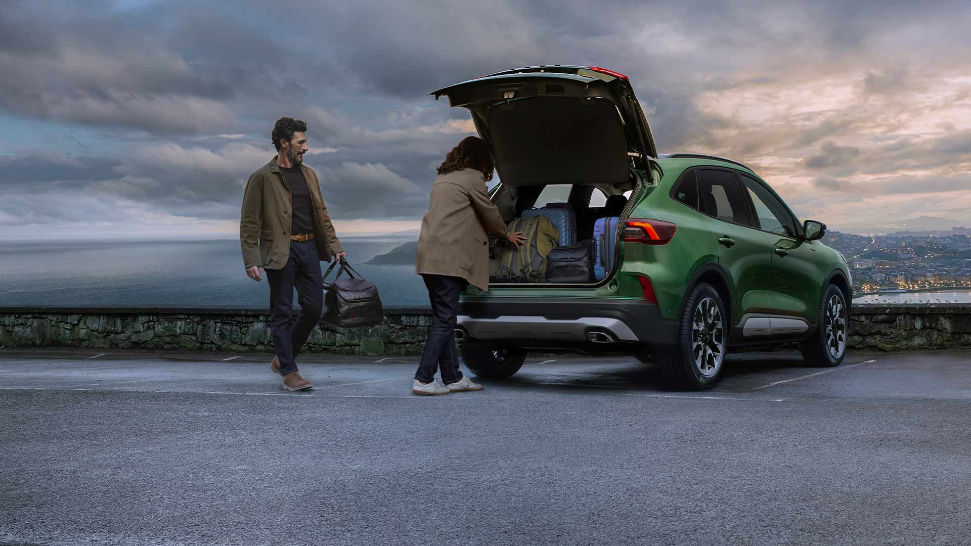 Due persone caricano diverse valigie nello spazioso vano portabagagli della Ford Kuga. 
