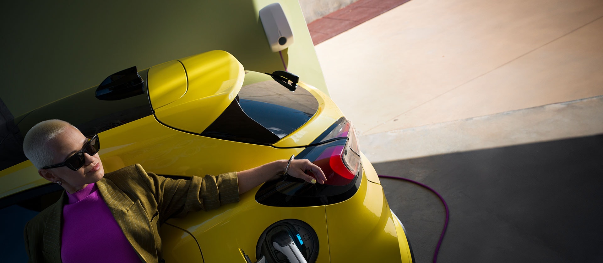 Primo piano della parte posteriore di una Ford Puma Gen-E® elettrica gialla, collegata a una Wallbox domestica.