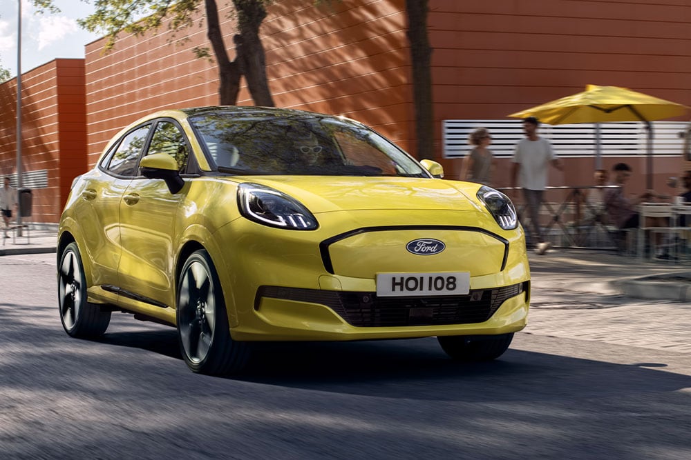Vista frontale di una Ford Puma Gen-E® elettrica gialla che percorre una strada cittadina.
