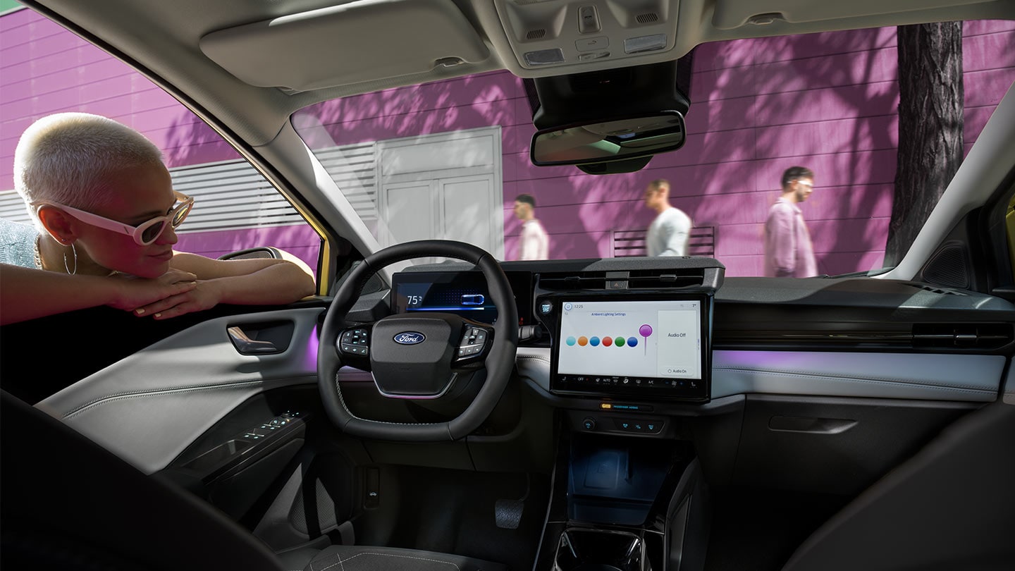 Persona che osserva gli interni della nuova Ford Puma Gen-E®, con il grande touchscreen e l'illuminazione ambiente.