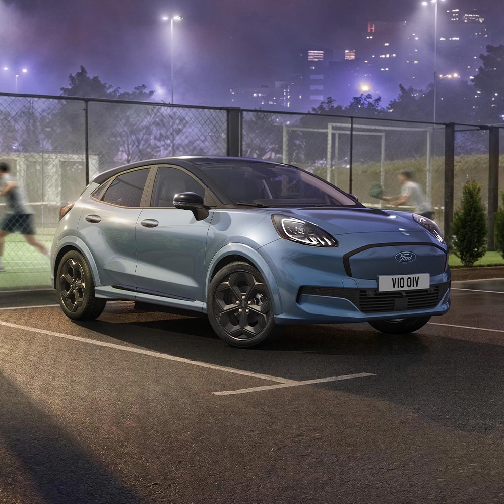 Una Ford Puma Gen-E disponibile in edizione limitata nel colore Vapor Blue con tecnologia BlueCruise, parcheggiata all’aperto vicino a un campo da padel.