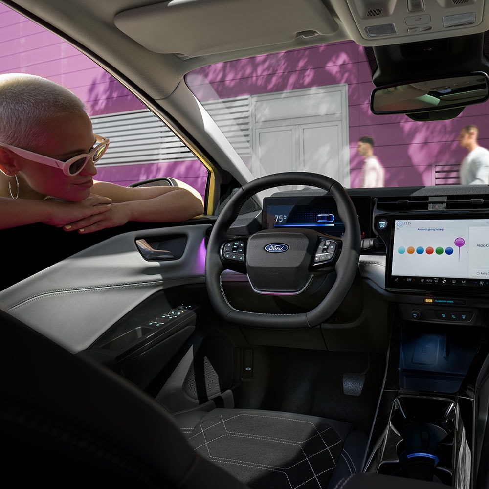Interni della Ford Puma Gen-E® elettrica, con una persona che guarda lo schermo dell'infotainment attraverso il finestrino.