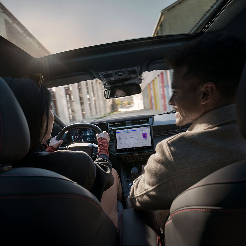 Il conducente e il passeggero chiacchierano durante la guida in un paesaggio soleggiato.
