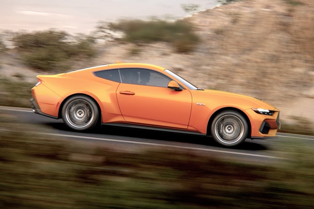 Vista laterale della Ford Mustang GT Fastback in vernice Orange Fury, che percorre una strada
