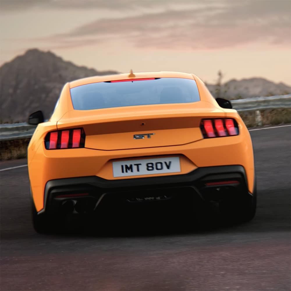Il retro di una Ford Mustang GT Fastback in vernice Orange Fury che affronta una curva stretta su una strada di campagna