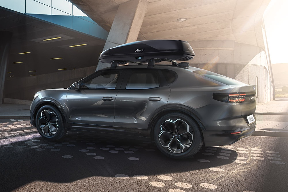 Vista 3/4 laterale di una Ford Capri scura con box da tetto, parcheggiata sotto una moderna struttura edilizia.