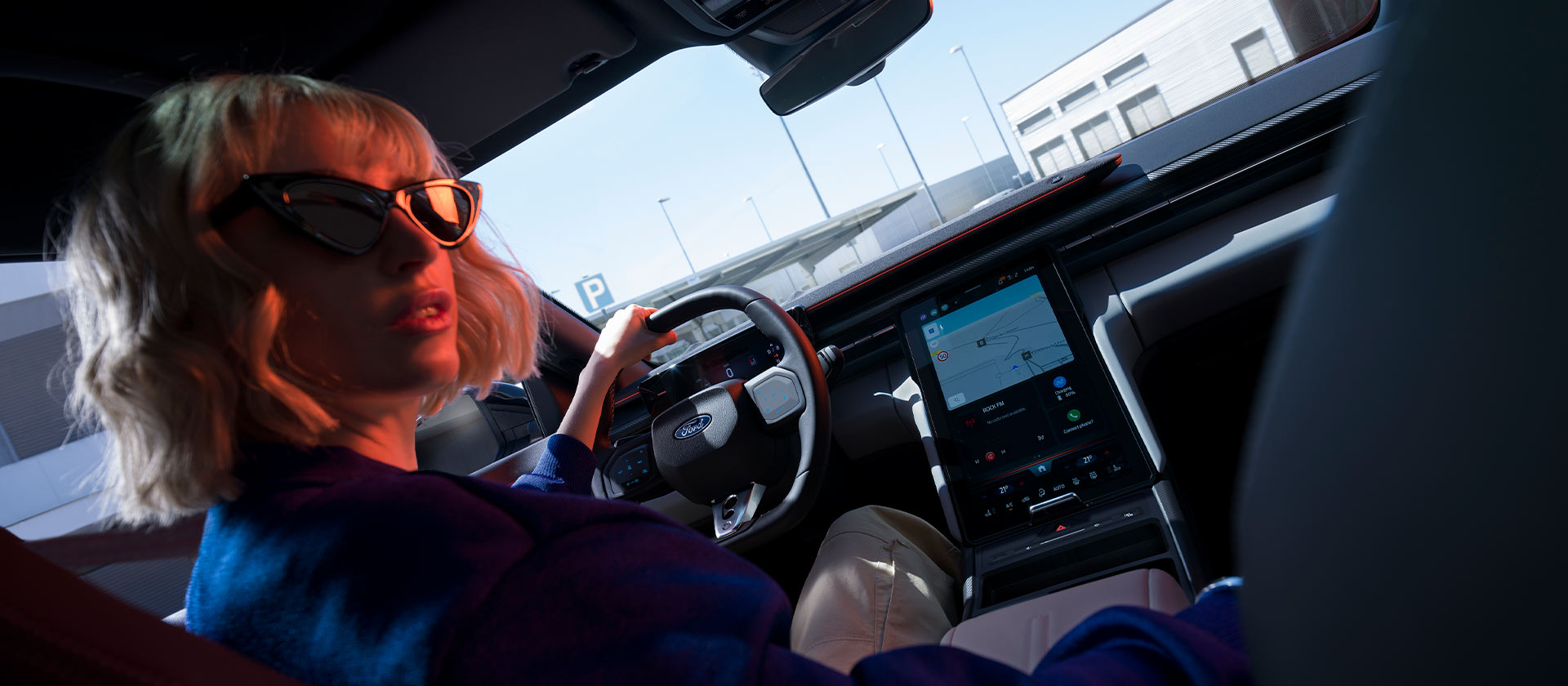 Una donna è seduta sul sedile di guida di una Ford Capri® parcheggiata, di cui sono visibili il volante e l’ampio touchscreen SYNC® Move.