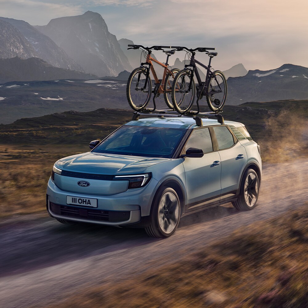 Ford Explorer blu su strada sterrata, con barre trasversali, portabici da tetto con due biciclette alloggiate.