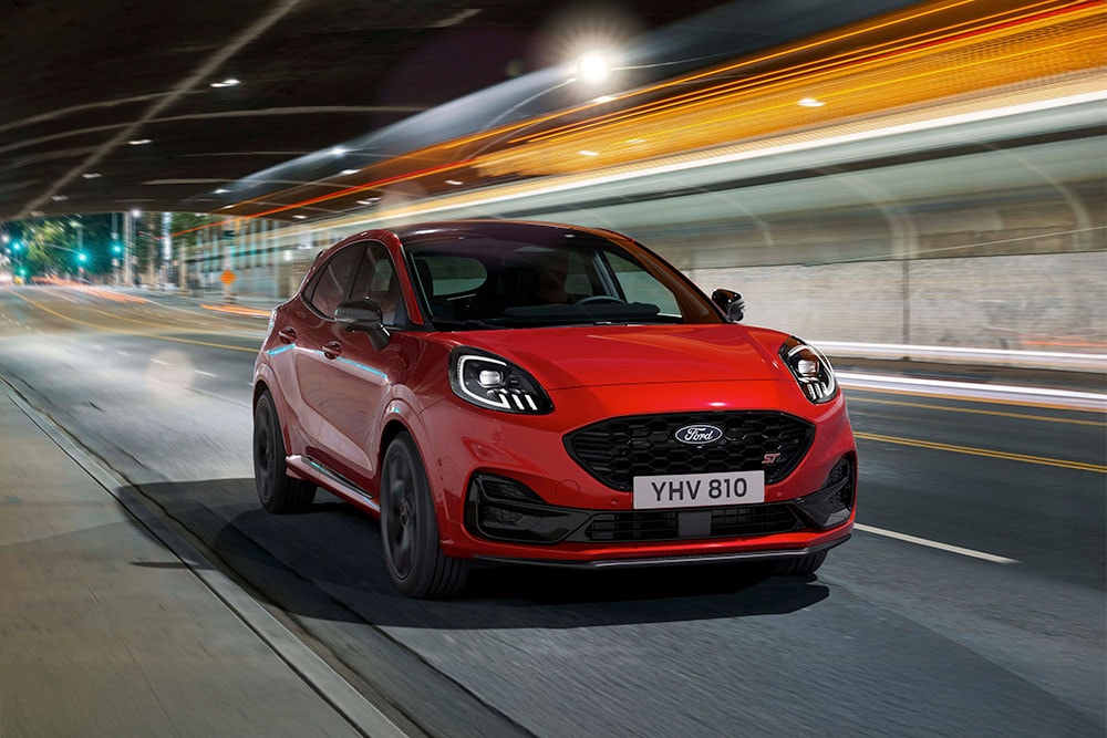 Un SUV sportivo  Ford Puma ST rosso che di notte percorre una strada cittadina illuminata.