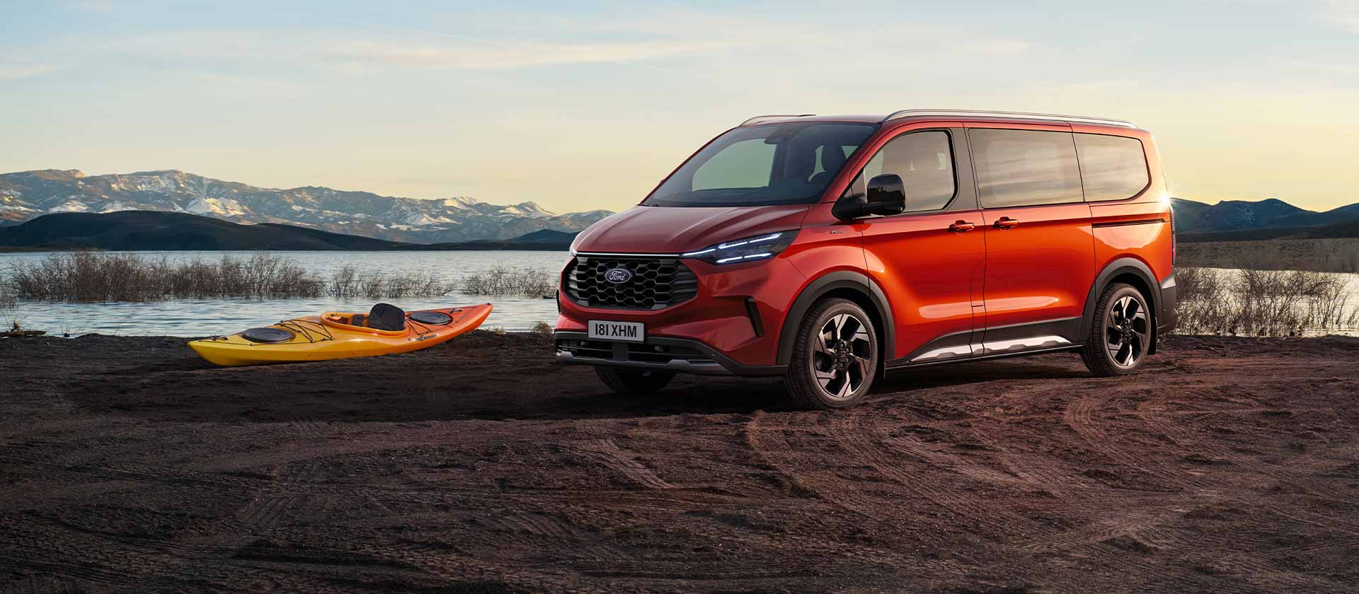 Ford Tourneo Custom rossa parcheggiata vicino a un lago con un kayak.