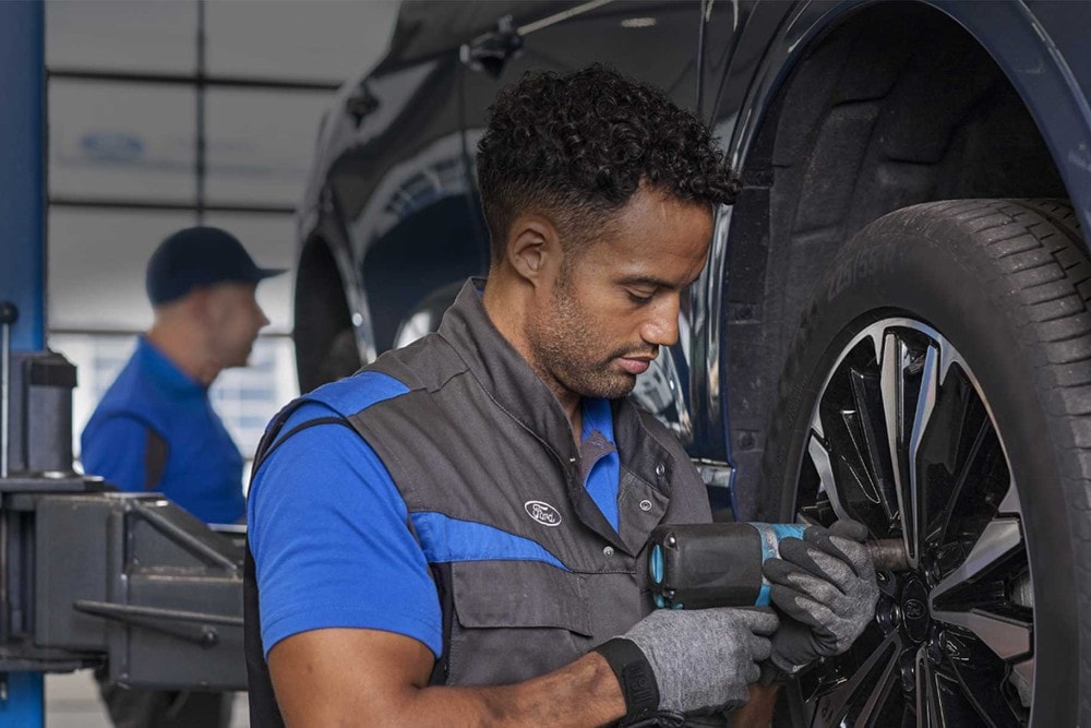 Un tecnico Ford usa un avvitatore a impulsi su una ruota, un collega lavora dietro.