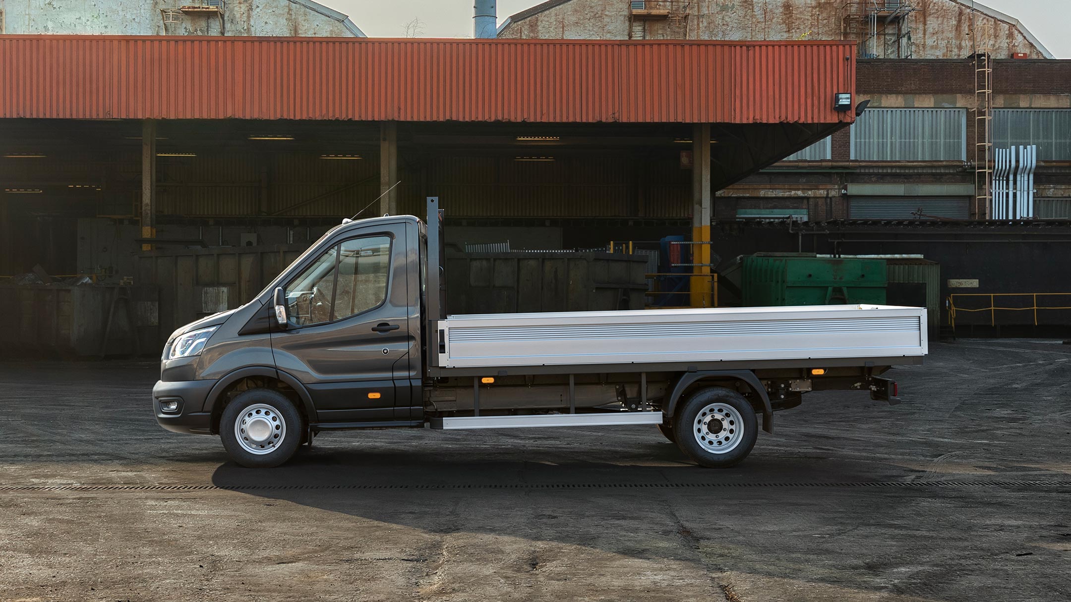 Ford Transit Chassis Cab da 5 tonnellate, nero, vista laterale, parcheggiato su un’area aziendale a fianco di una tettoia con pallet 