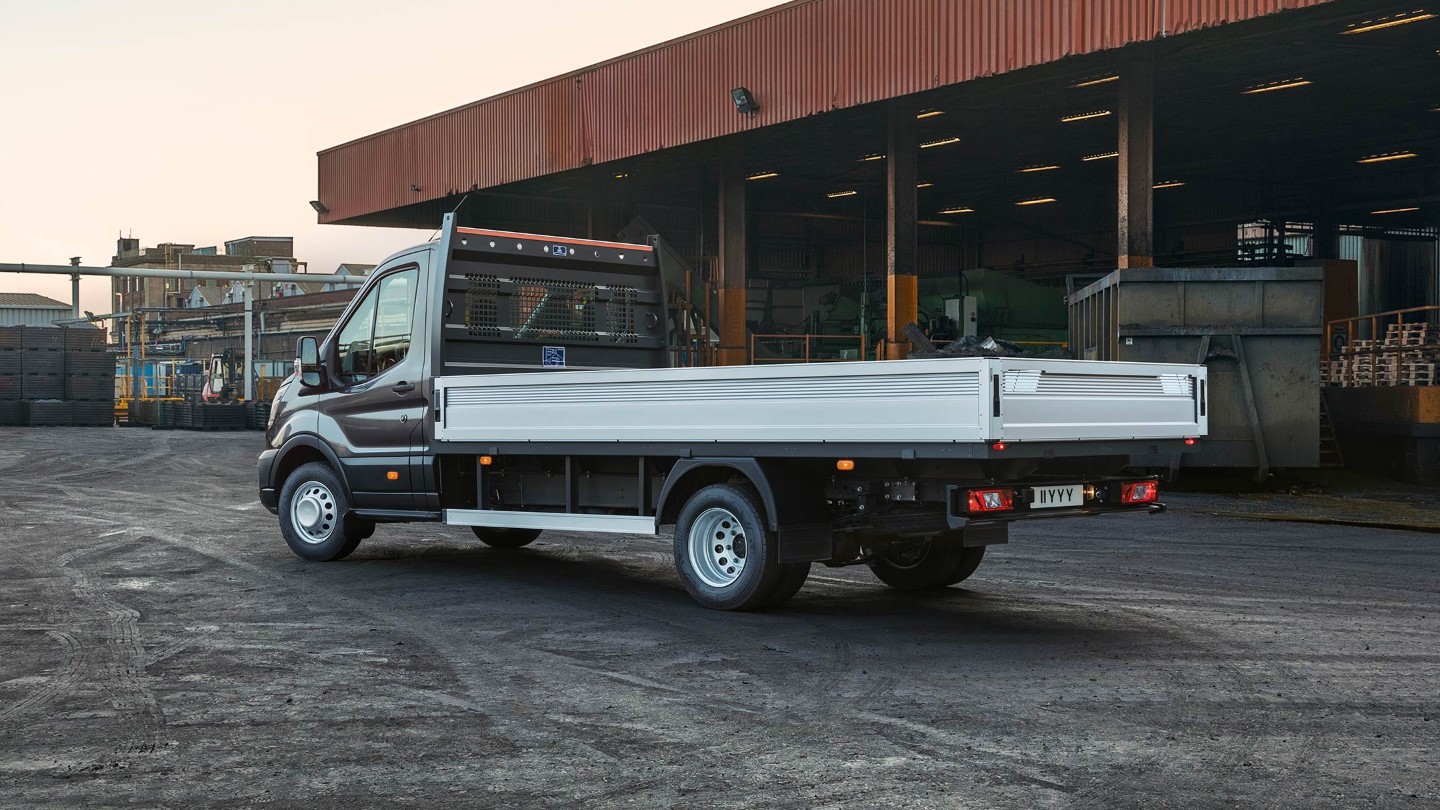 Ford Transit 5 tonnellate a pianale piatto Nero ¾-vista posteriore parcheggiato nei locali dell'azienda accanto alla copertura con pallet Ford Transit 5 tonnellate a pianale piatto Nero ¾-vista posteriore parcheggiato nei locali dell'azienda accanto alla copertura con pallet
