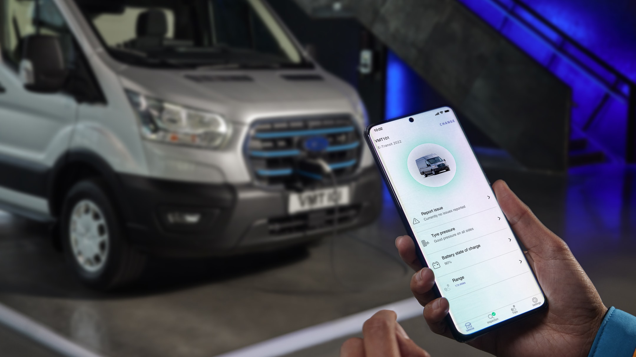 Particolare della vista frontale a tre quarti del Ford E-Transit color argento, con mano che regge uno smartphone