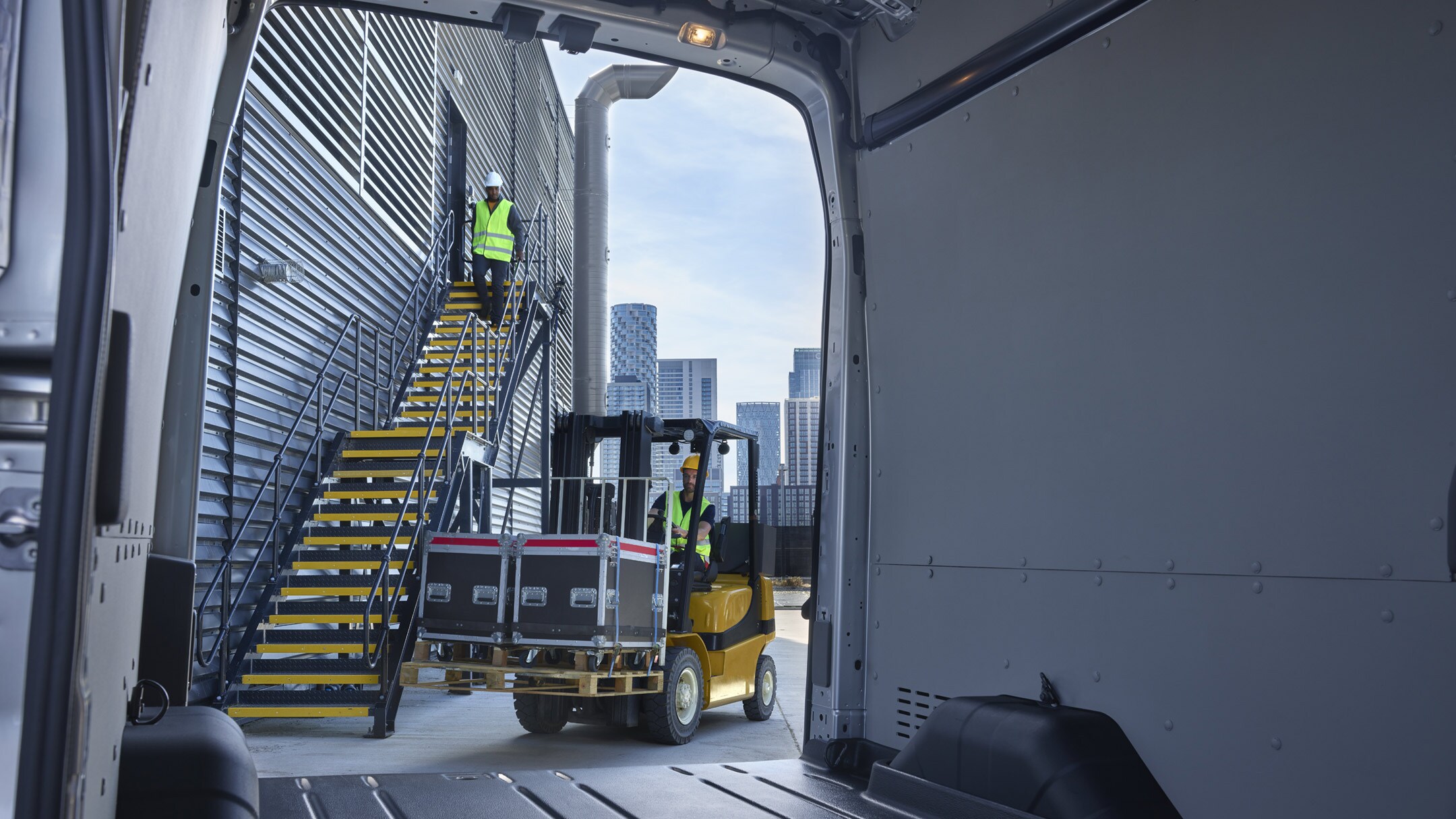 Vista attraverso il portellone posteriore aperto dal vano di carico del Ford E-Transit furgone cabinato su un carrello elevatore carico sullo sfondo