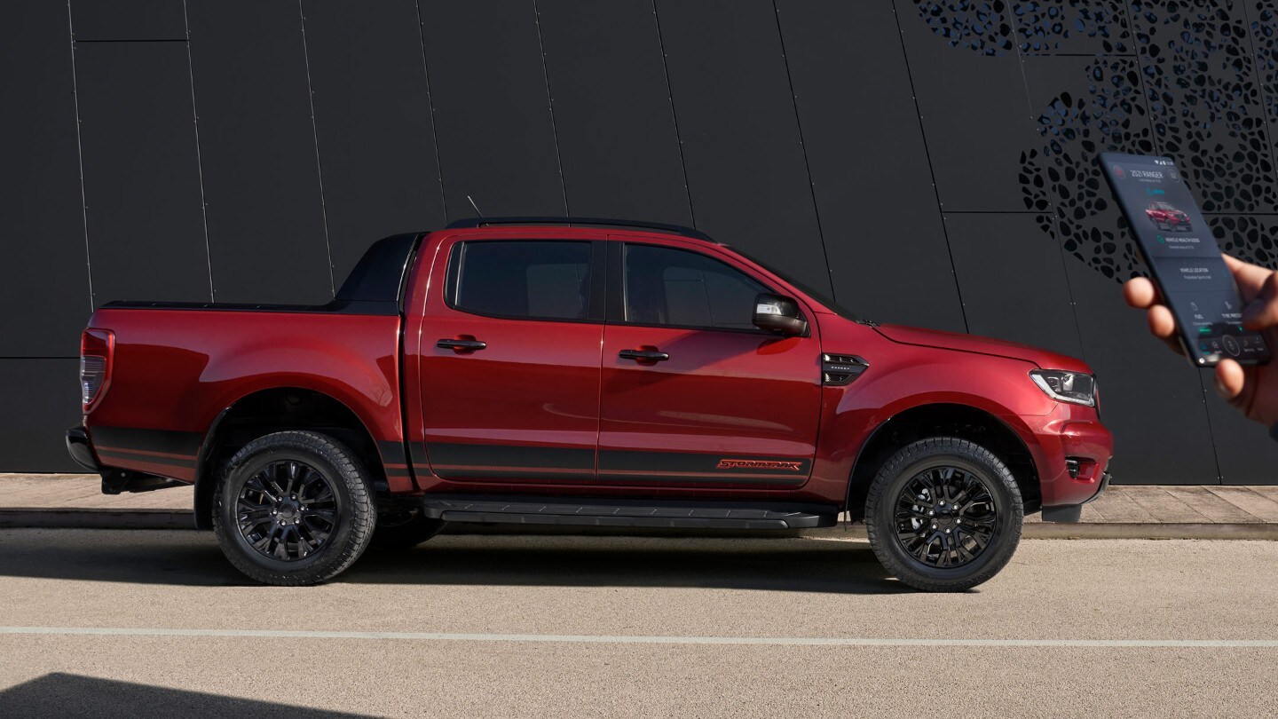 Ford Ranger Stormtrak rosso, vista laterale, parcheggiato, mentre una mano impugna un cellulare
