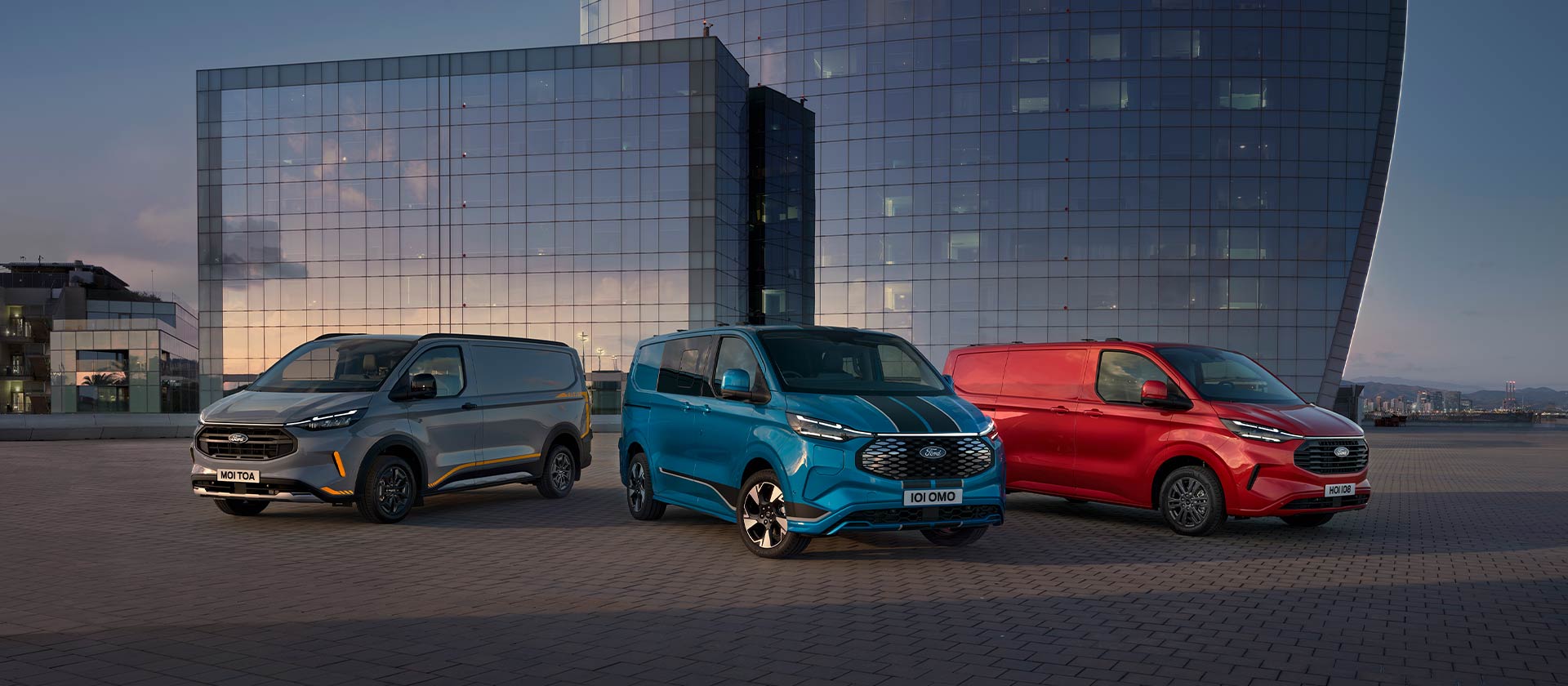 Tre furgoni Ford Transit Custom Sport nei colori grigio, blu e rosso parcheggiati.