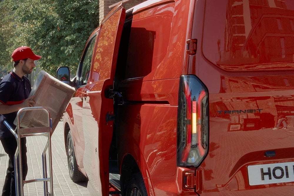 Un corriere scarica dei pacchi da un Ford E-Transit Custom rosso.