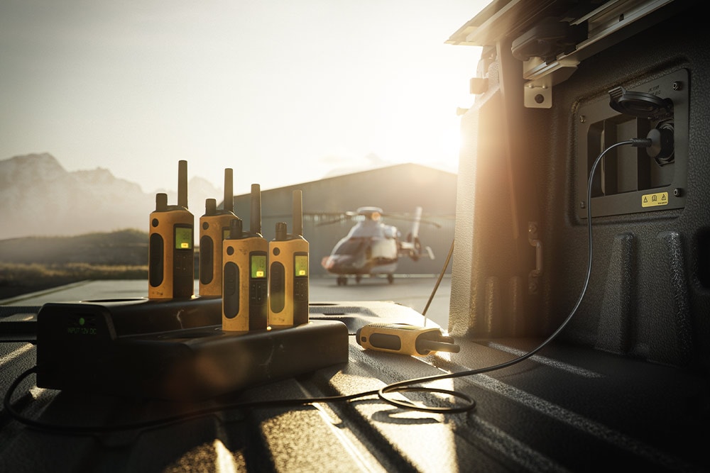 Diversi walkie-talkie in carica nel cassone di un Ranger Raptor al tramonto, con un elicottero in lontananza.