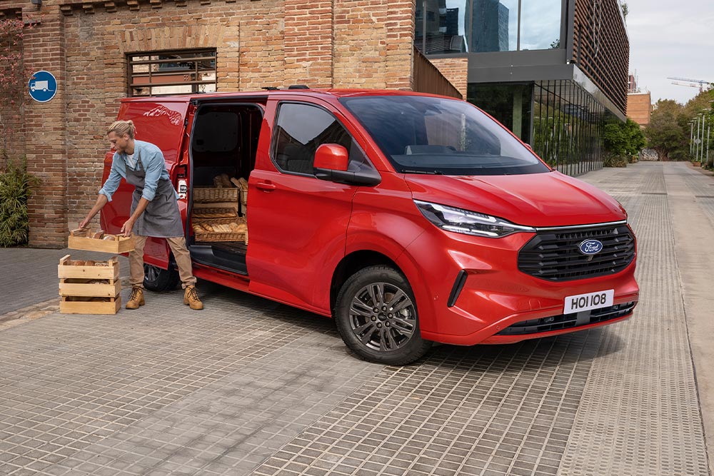 Autista delle consegne che carica pacchi attraverso la porta laterale di un Ford Transit Custom rosso.