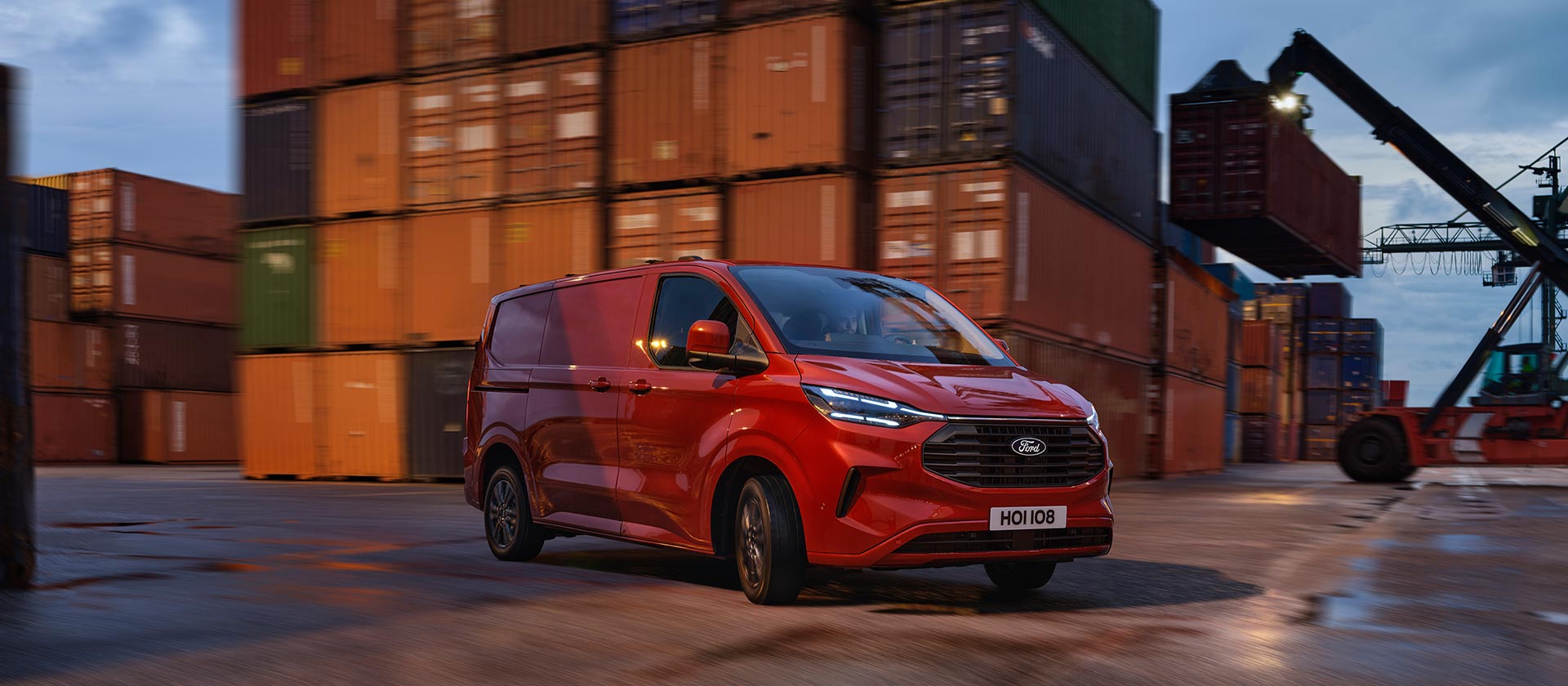Red Ford Transit Custom van drives through a dock yard.