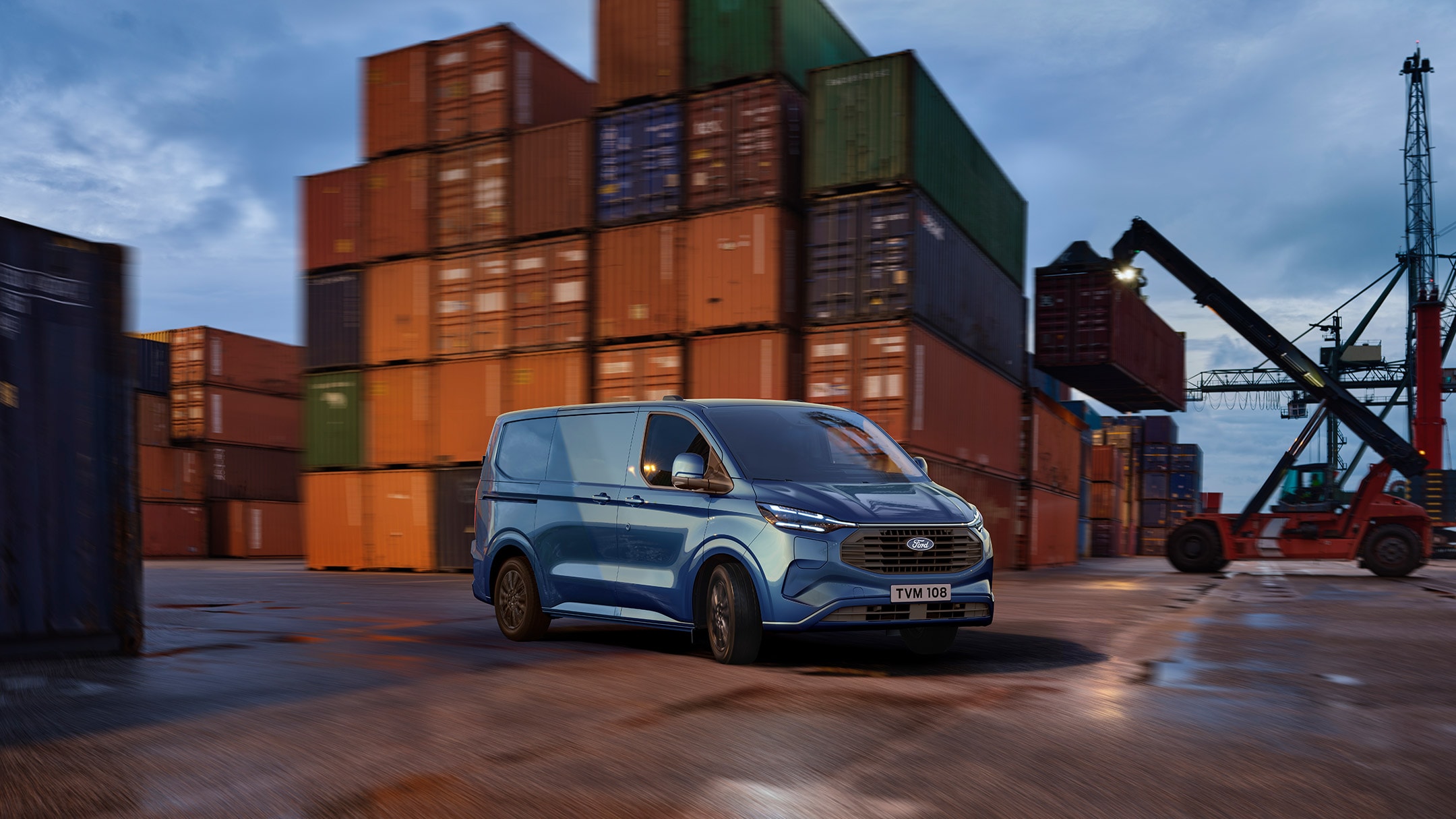 Ford Transit Custom Plug-In Hybrid blu in un terminal container tra i container al tramonto.
