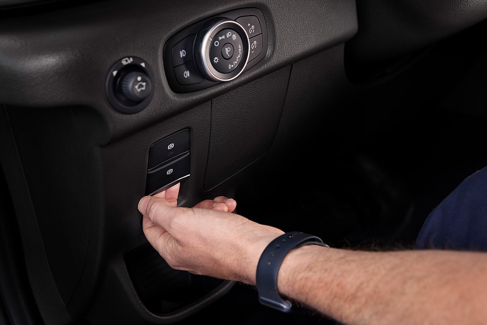 Primo piano di una mano che preme un pulsante sul cruscotto di un furgone elettrico Ford E-Transit.