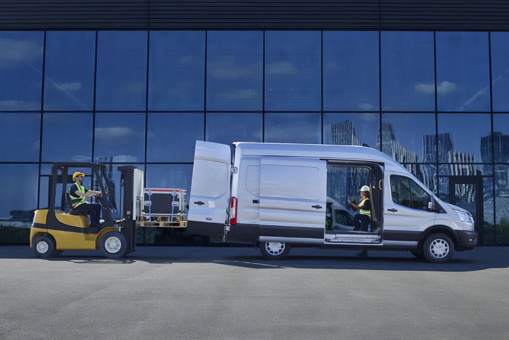 Due persone che caricano il carico su un furgone Ford Transit di color argento con un carrello elevatore.