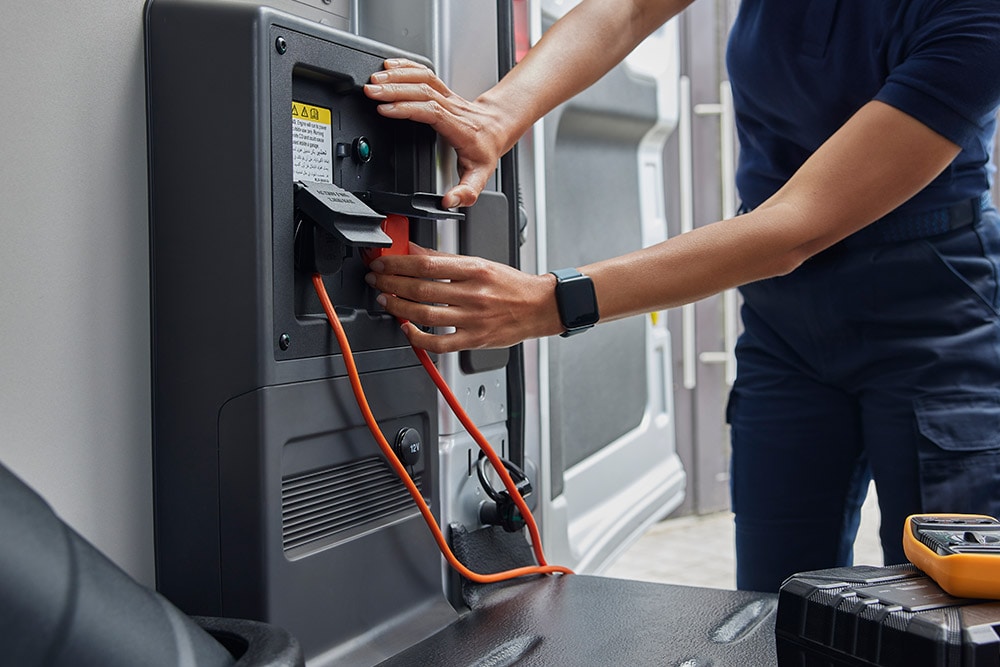 Primo piano di una persona che collega un cavo di ricarica all'interno di un furgone elettrico Ford E-Transit.