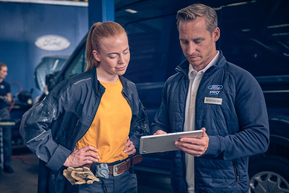 Due meccanici in un garage che guardano un tablet di fronte a un furgone Ford E-Transit.