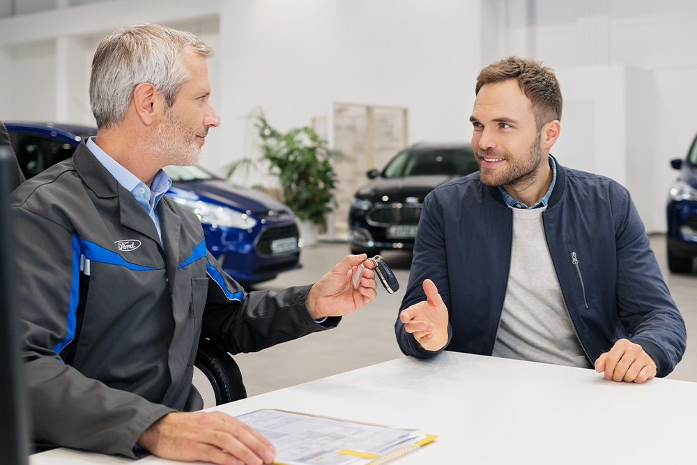 Un consulente Ford consegna le chiavi a un cliente mentre discute le opzioni di finanziamento Ford disponibili.