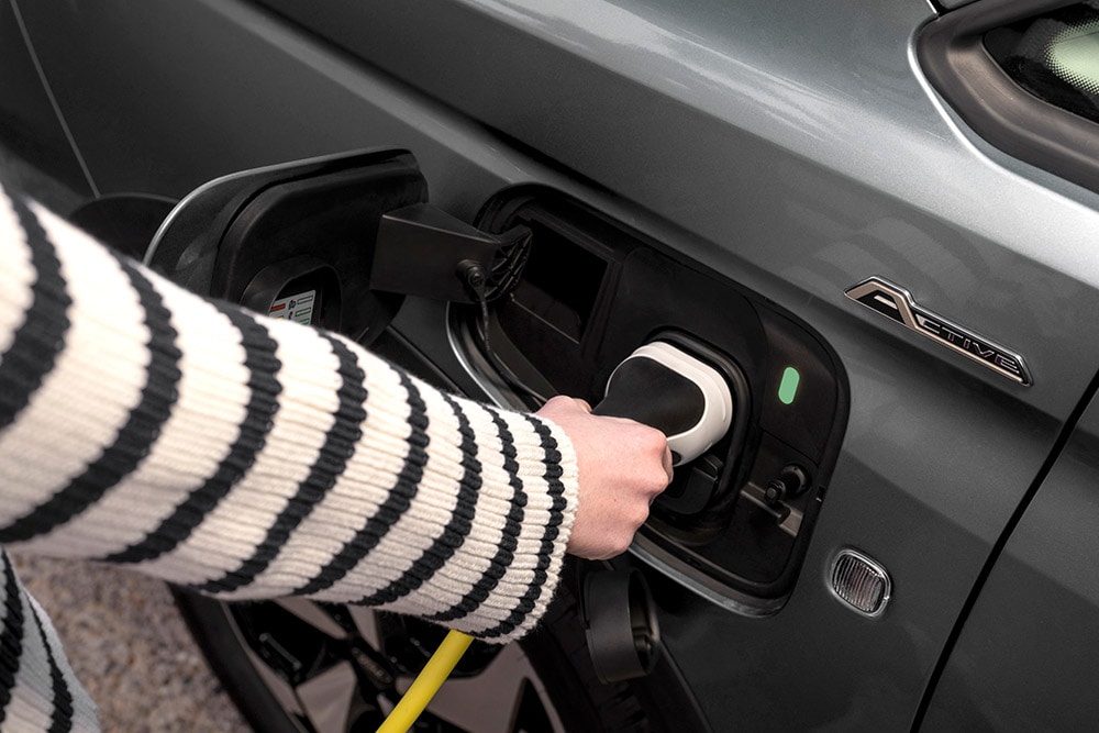 Una persona che collega un cavo di ricarica a un Ford Transit Connect ibrido plug-in.