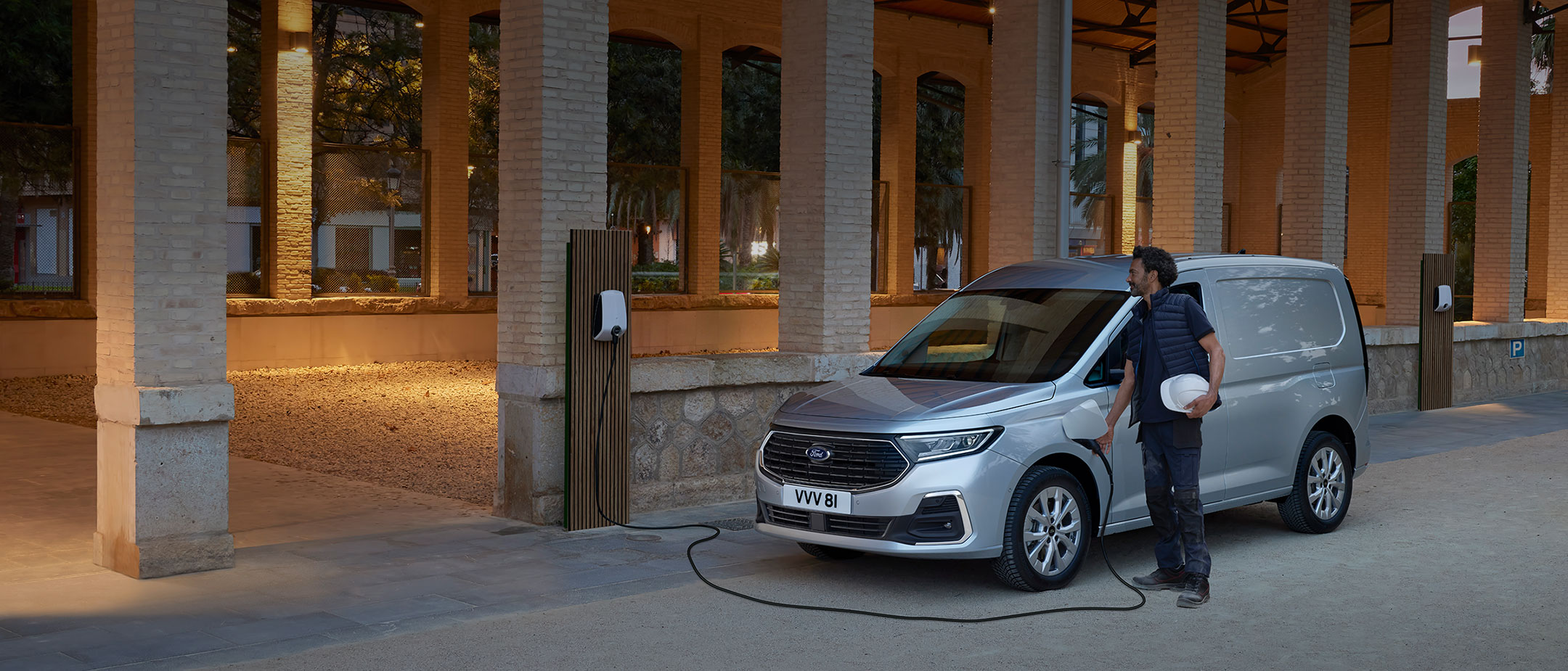 Un uomo con indosso un casco collega il cavo di una Wallbox a un Ford Transit Connect color Stardust Silver.