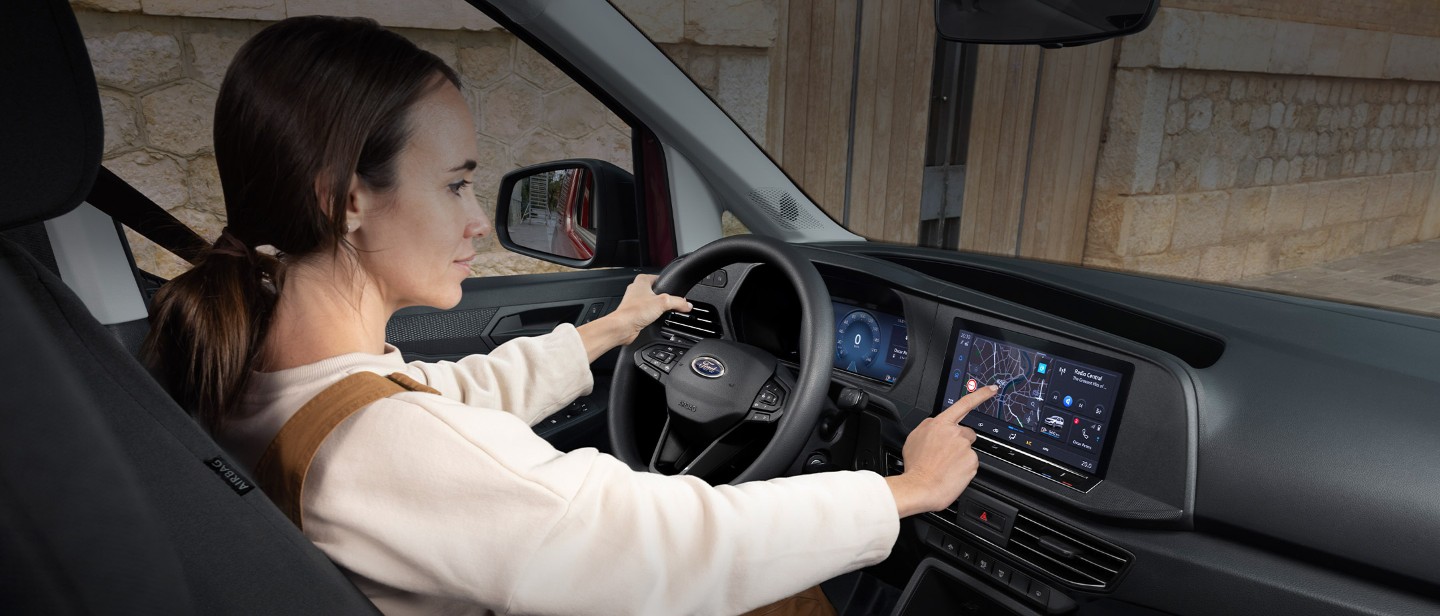 Una donna seduta al posto di guida del Ford Transit Connect tocca un touchscreen da 10 pollici.
