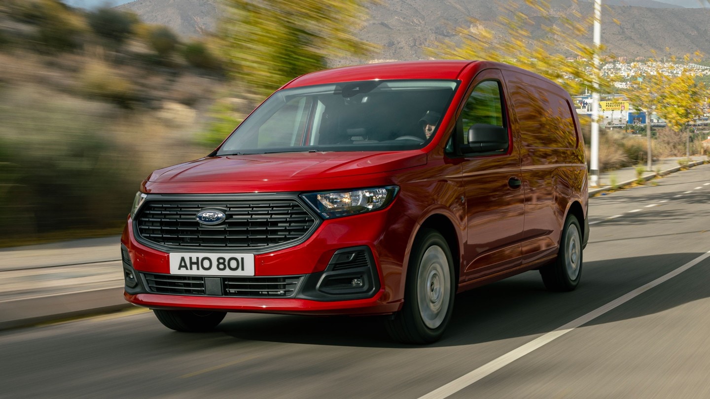 Ford Transit Connect color Maple Red con calandra e fari, in marcia lungo una strada.