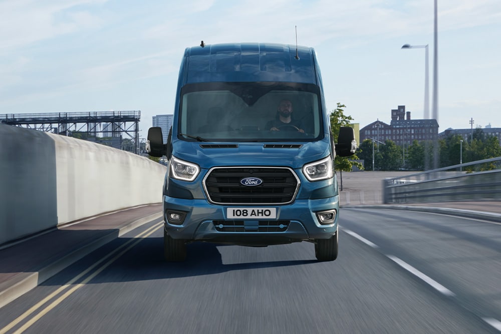 Vista frontale del Ford Transit Van blu che percorre una strada. 