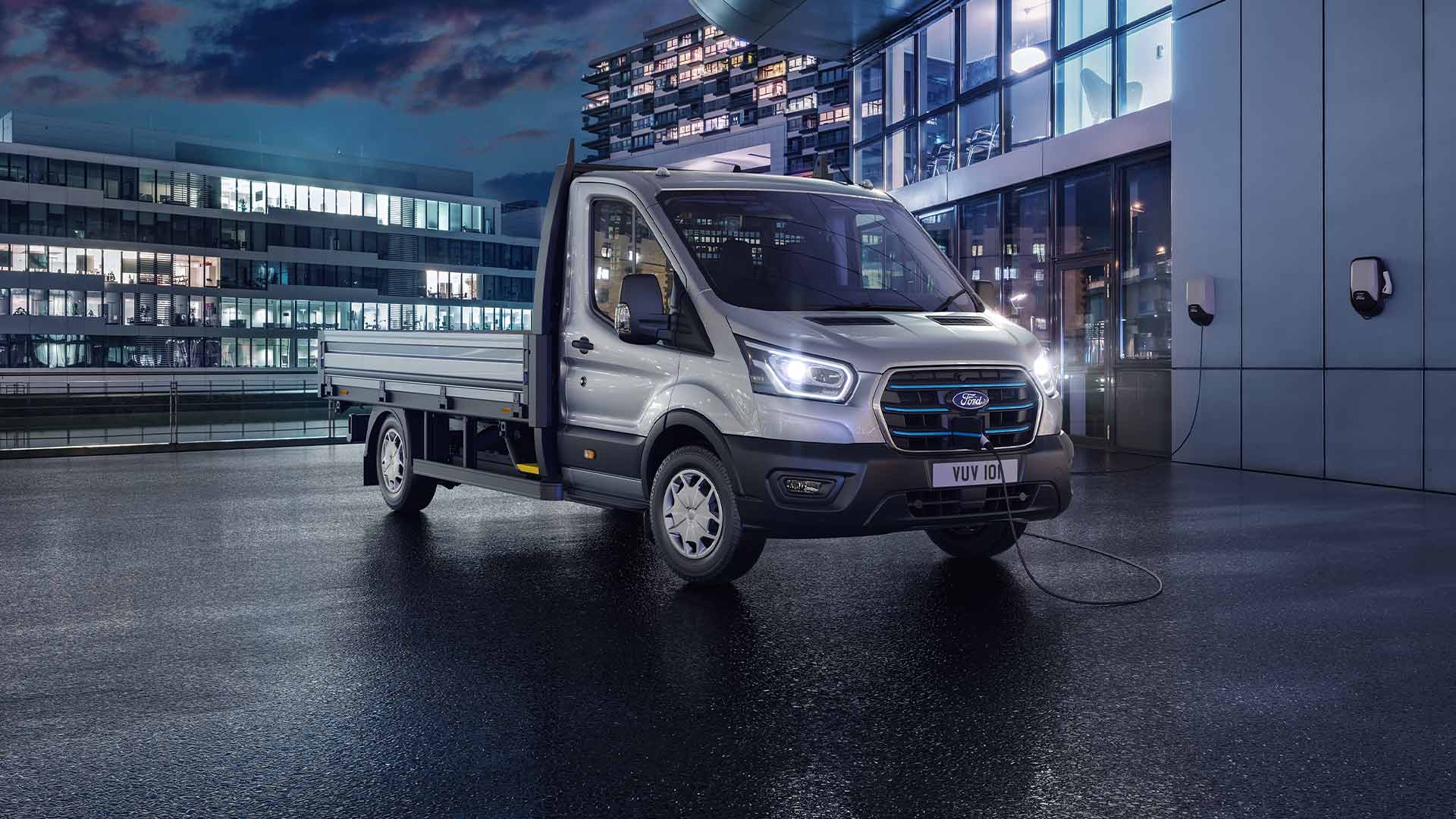 Ford E-Transit Chassis Cab argento parcheggiato di notte di fronte a un edificio moderno.