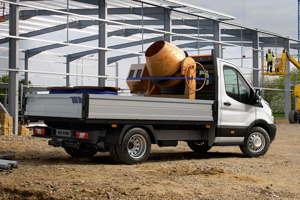 Ford Transit Chassis Cab che trasporta una betoniera sul piano di carico, parcheggiato in un cantiere. 