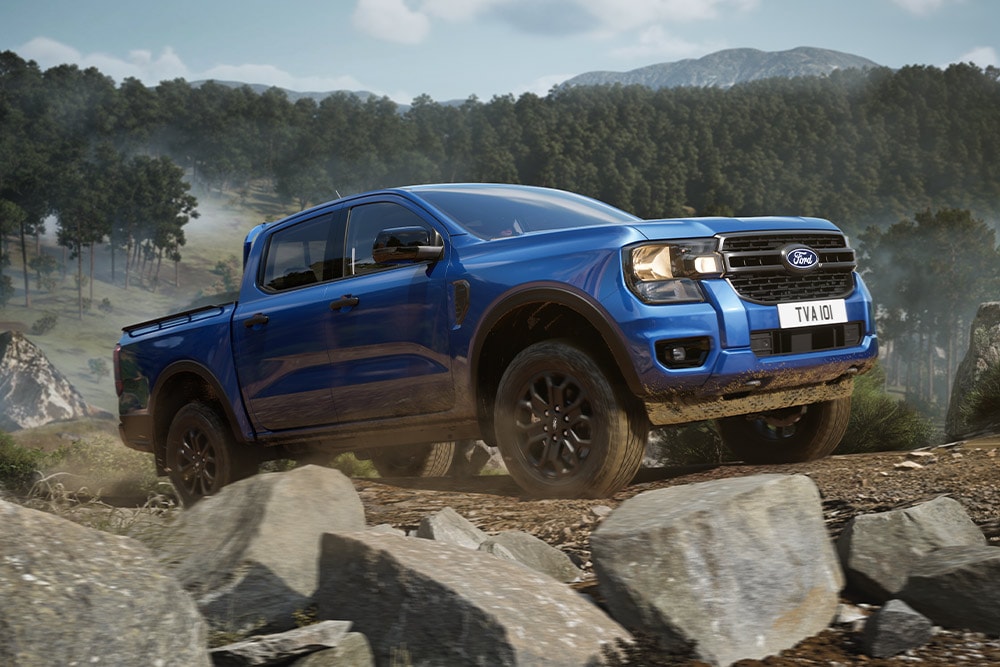 Un pick-up Ford Ranger blu percorre una strada sterrata in una foresta, lasciando una scia di polvere.