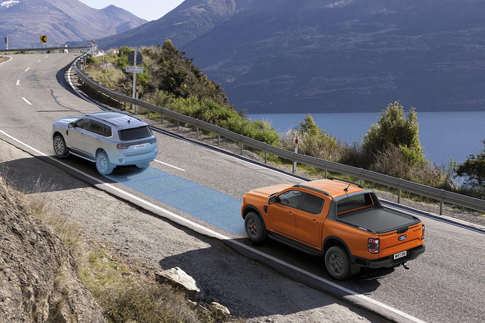 Un Ford Ranger arancione utilizza l’avanzato sistema di assistenza alla guida lungo un’autostrada costiera.